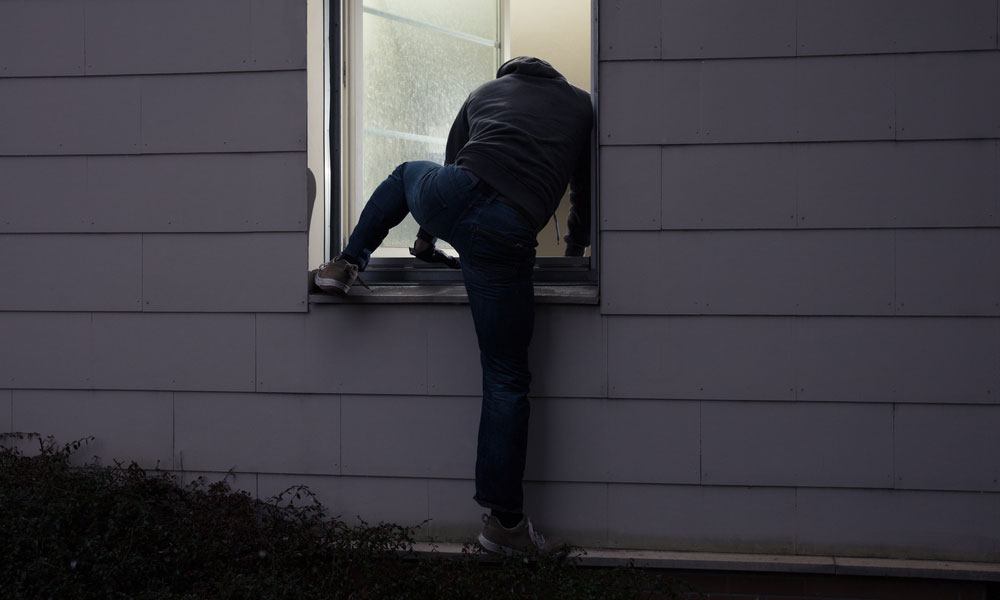 Burglar in black hoodie climbing into an unsecured window in home