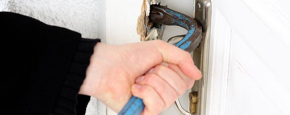 burglar bbreaking into door using a blue crowbar